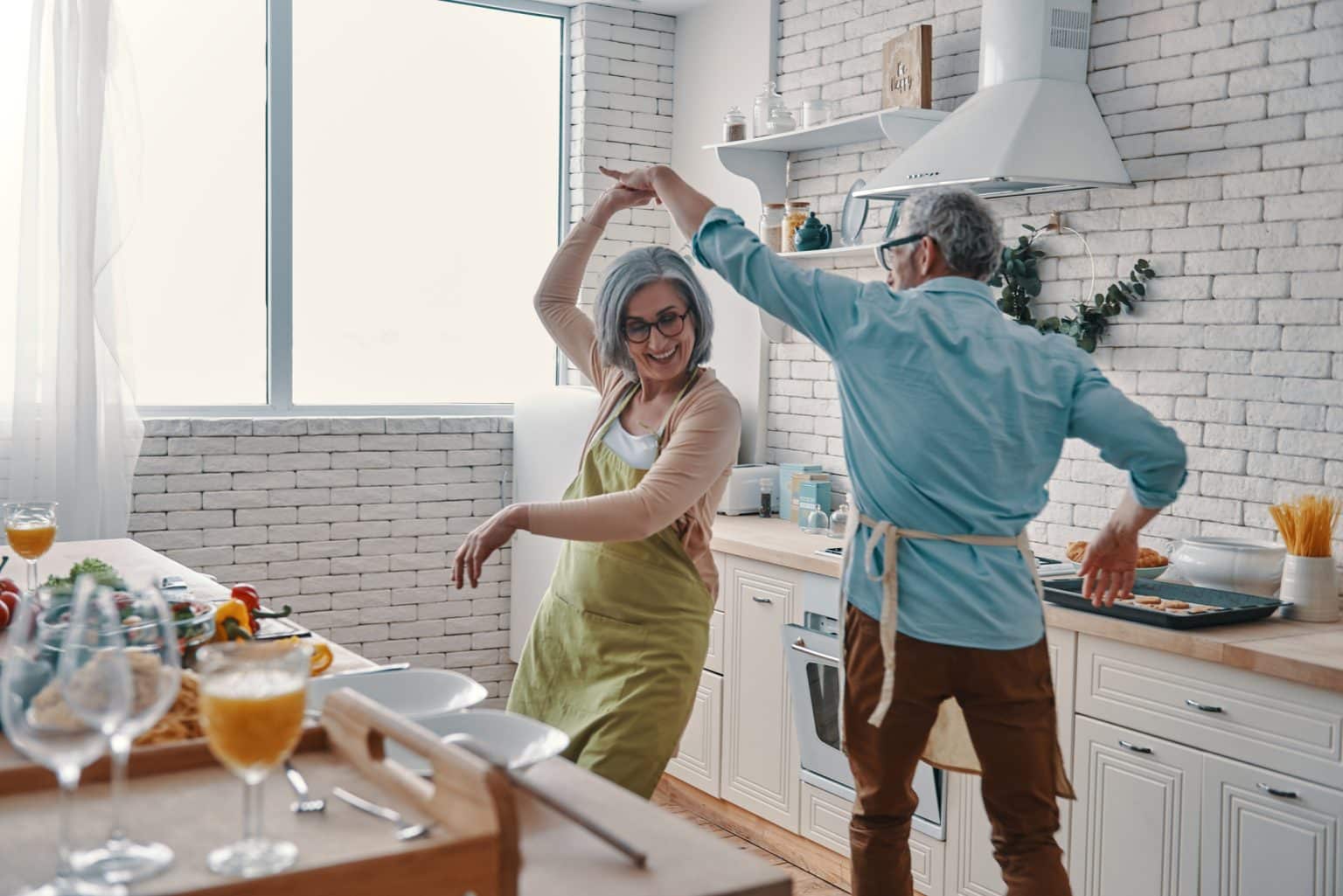 Older woman and her husband dancing in the kitchen while preparing dinner.