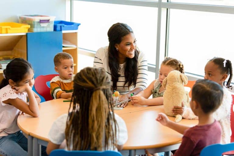 Teacher sits at table with young children providing early learning while using a three dimensional diagram of the solar system as a teaching aid